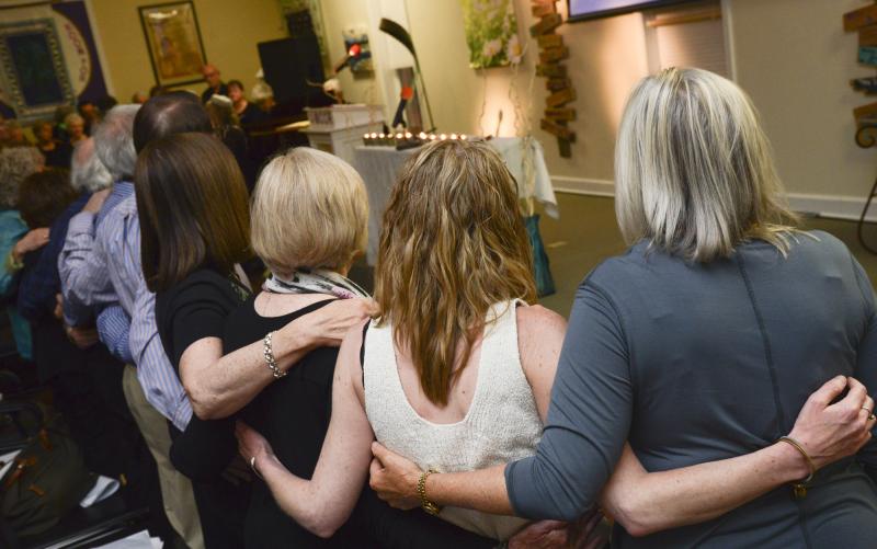 A group embraces and sings a song of remembrance after many in the congregaton shared stories of the Holocaust that touched their lives.